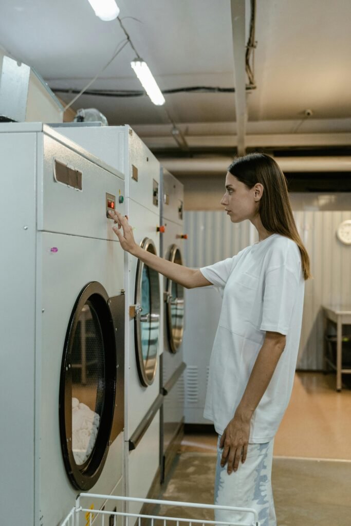 A young woman operates a washing machine in a self-service laundromat, performing routine laundry tasks.